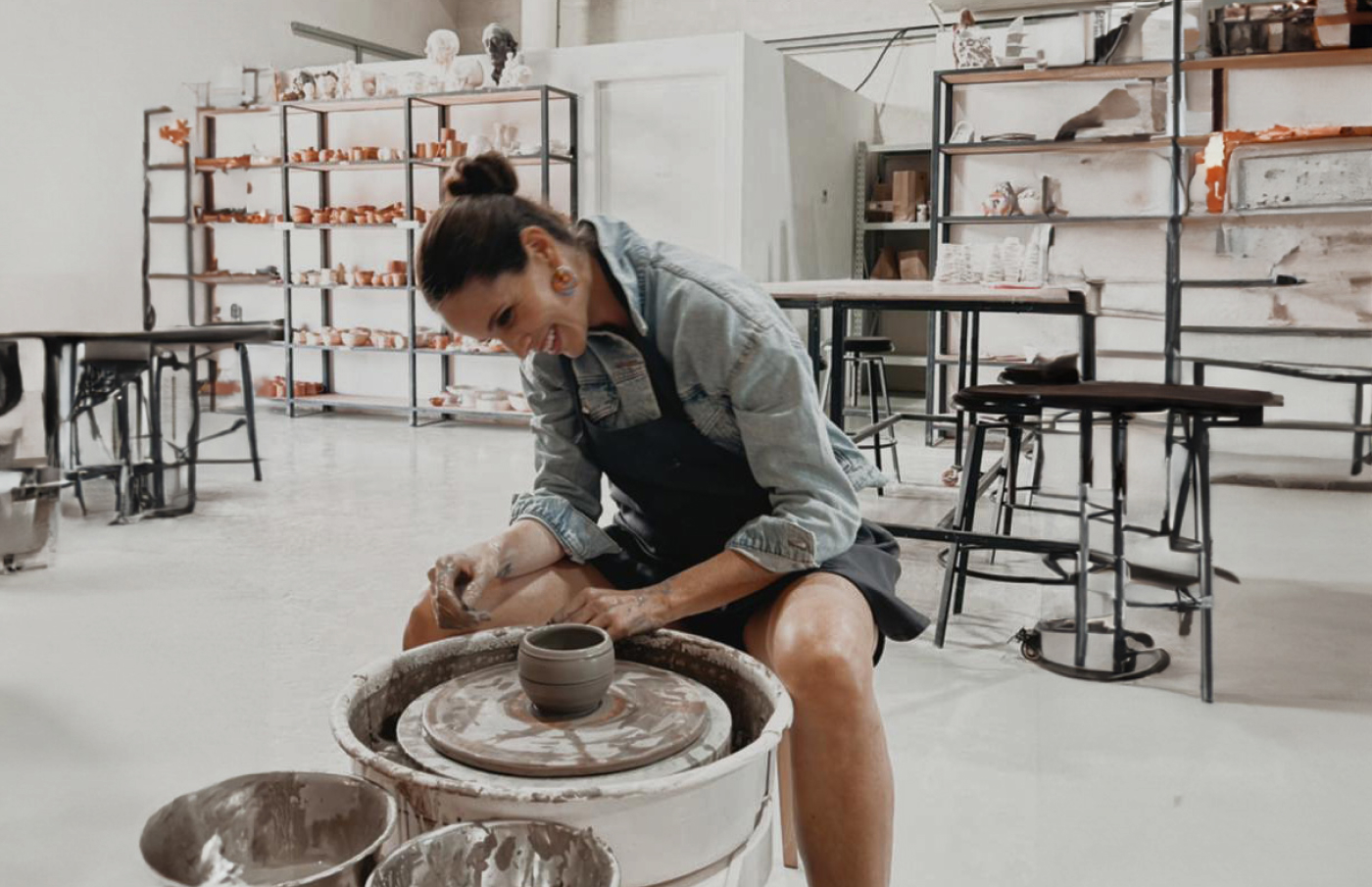 Chiara in a ceramics and pottery studio, laughing while shaping clay with her hands.