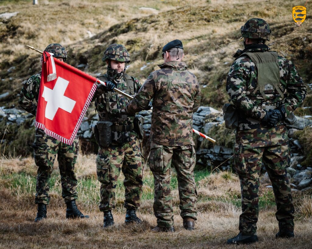 Michael Savolainen (second left) holds the Swiss flag while wearing camouflage and stands amidst a group of four men